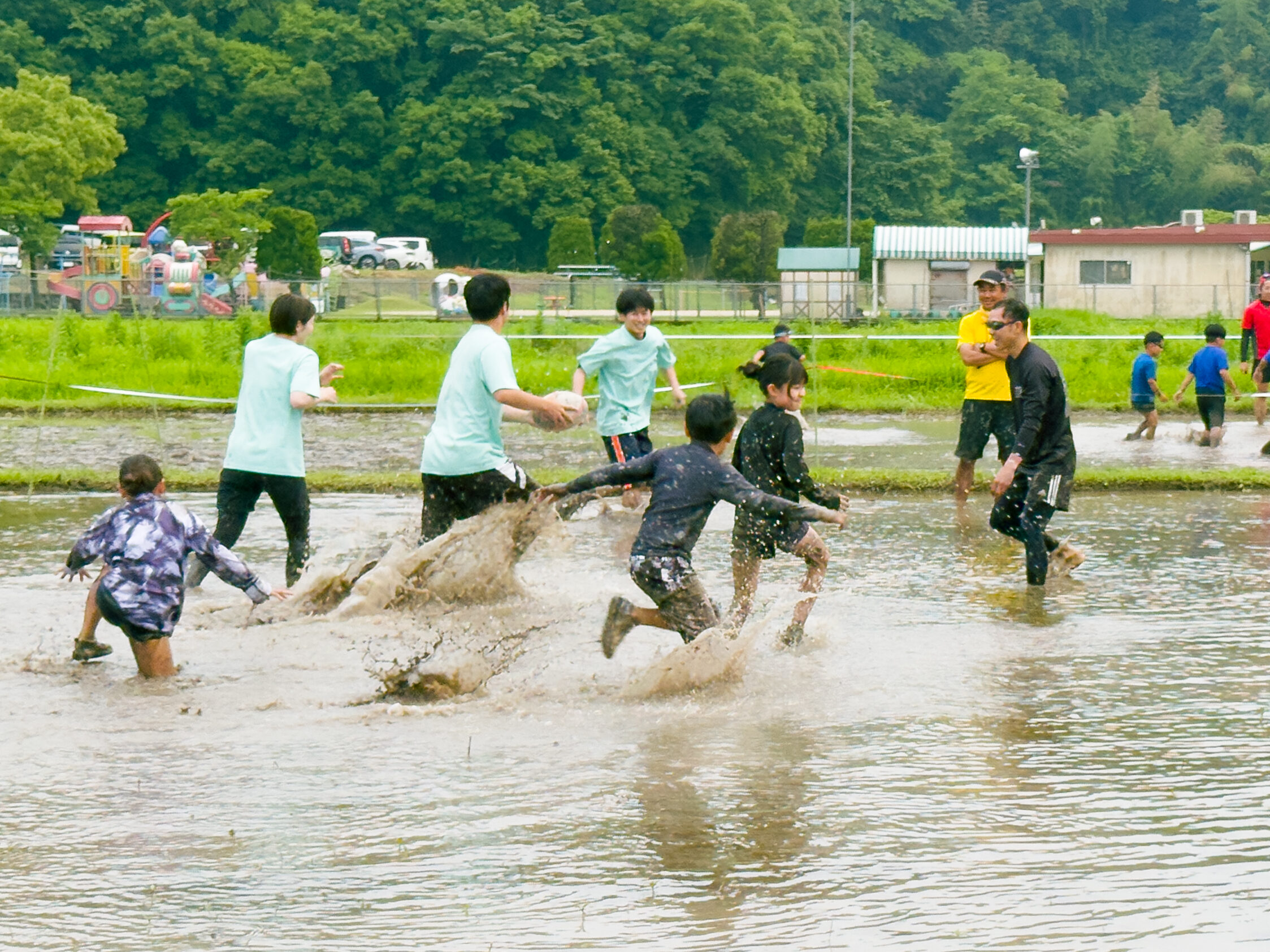 田んぼラグビー体験で、子どもたちが泥しぶきを上げながらボールを追う